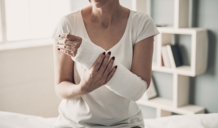 Caucasian Injured Woman in White T-Shirt Sitting and Holding Wrist in Gypsum Bandage